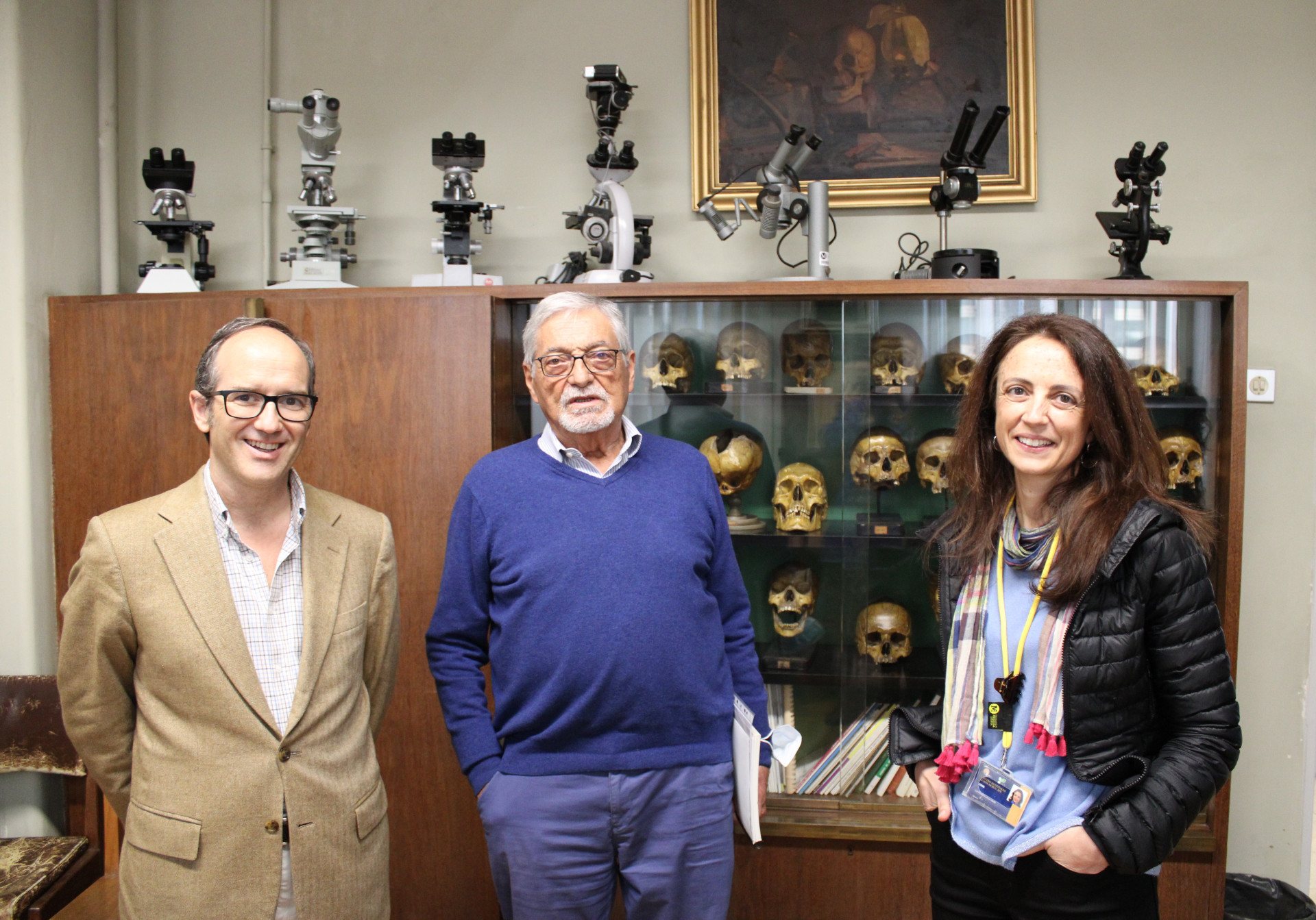 dois homens e uma mulher sorriem em frente de montra com crânios antigos, que eram usados para estudar anatomia