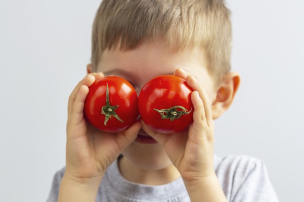 criança segura tomates maduros diante dos olhos 