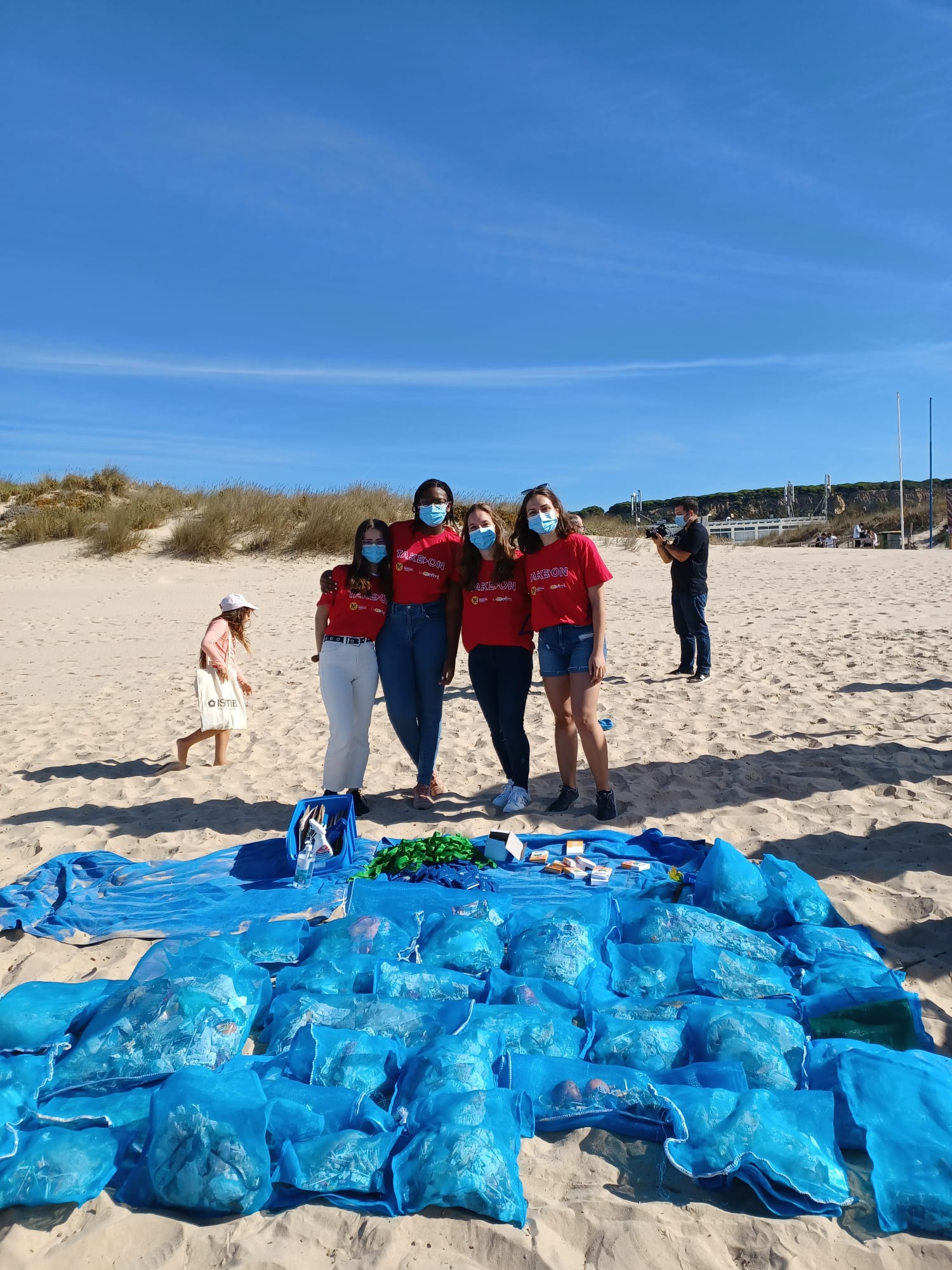 4 jovens numa praia com muitos sacos de lixo recolhido do areal à sua frente
