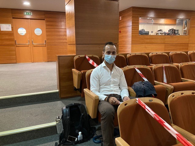 Homem de máscara sentado num auditório