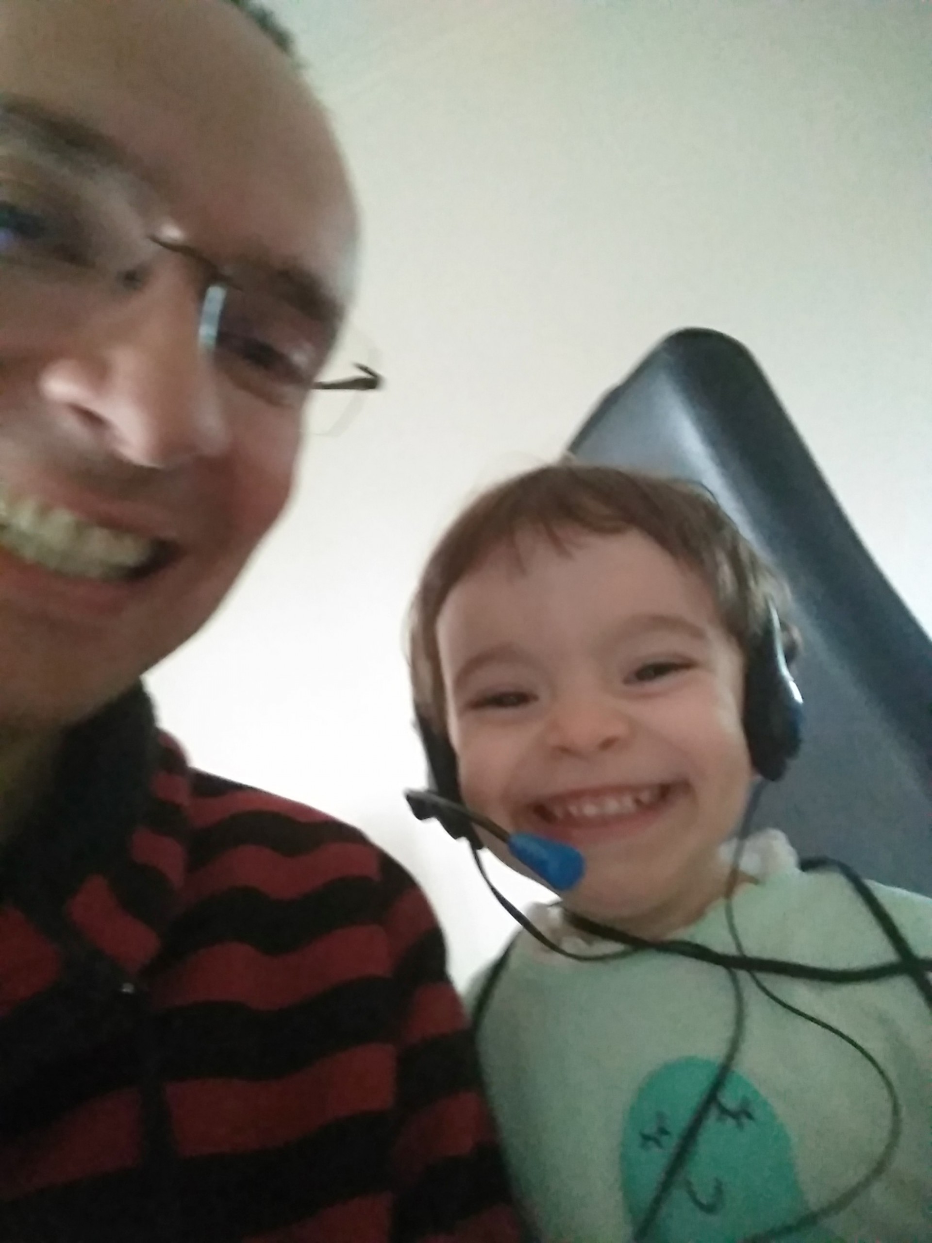 selfie de homem em regime de teletrabalho com filha de 2 anos. A menina sorri com os headsets do pai