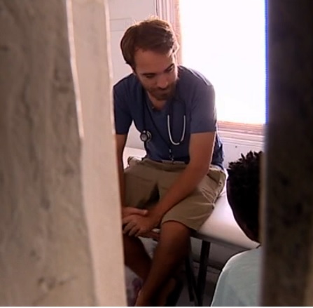 O Sebastião a dar uma consulta, durante o seu voluntariado médico. Está sentado numa mesa, e tem à sua frente um paciente.