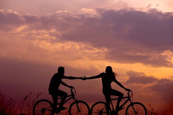 2 jovens a andar de bicicleta e de mãos dadas