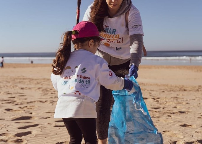 menina pequenina coloca no saco de lixo um pedaço de plastico apanhado do areal da praia