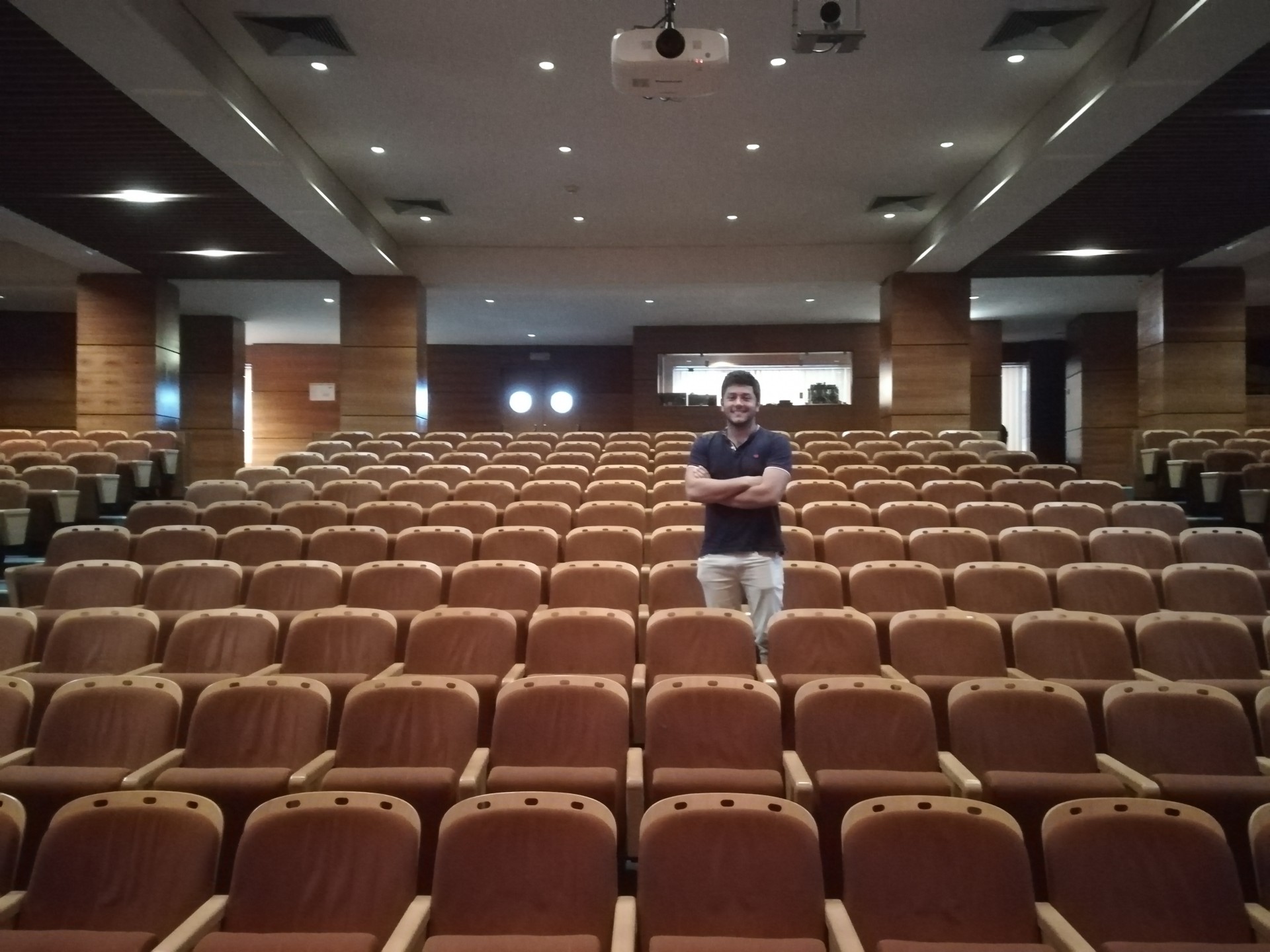 rapaz em pé entre cadeiras de um auditório